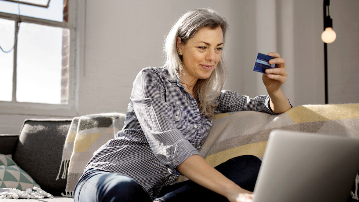 Femme mûre choisissant la carte de débit comme mode de paiement tout en utilisant un ordinateur portable.