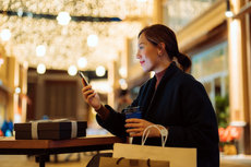 Asian woman looking at her phone as she's in a festive environment with shopping bags