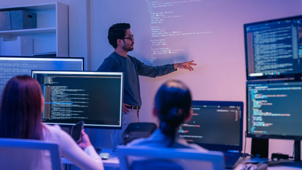 Tech team collaboration during code review session with multiple monitors
