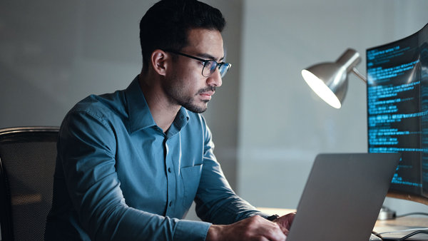 IT professional reviewing programming code on dual displays