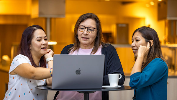 hree women engaged in conversation while looking at a laptop screen