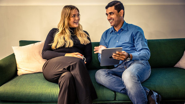 A man and woman sitting on a sofa engaged in conversation, with the man holding a tablet