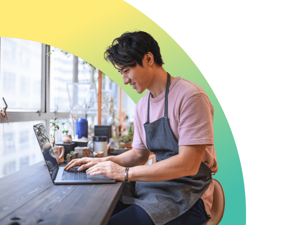 Young businessman using laptop at table smiling wearing apron