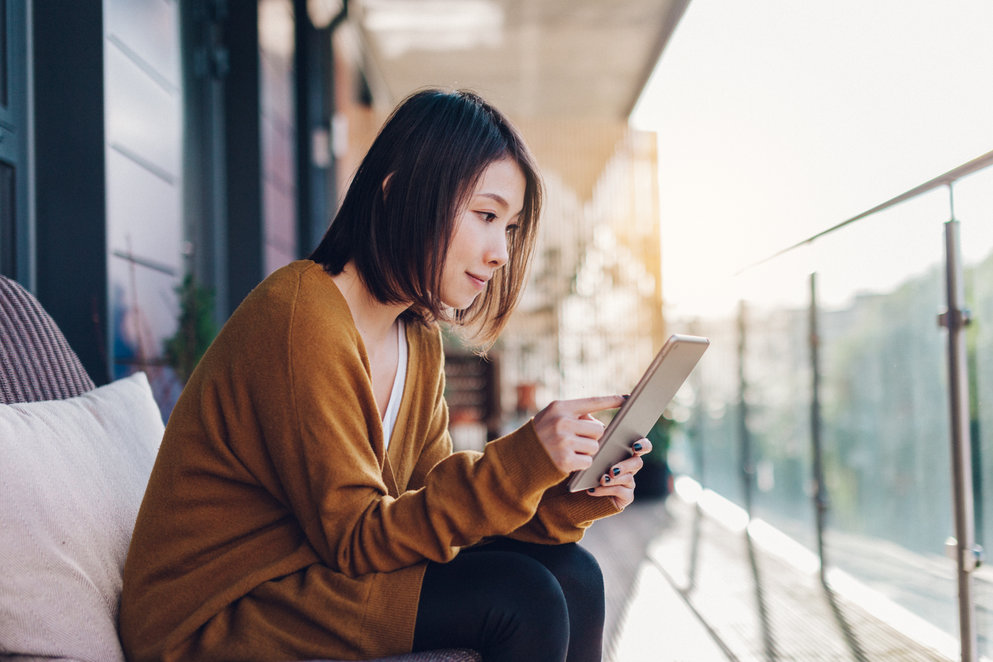 Asian woman checking content on her tablet while sitting at a balcony.