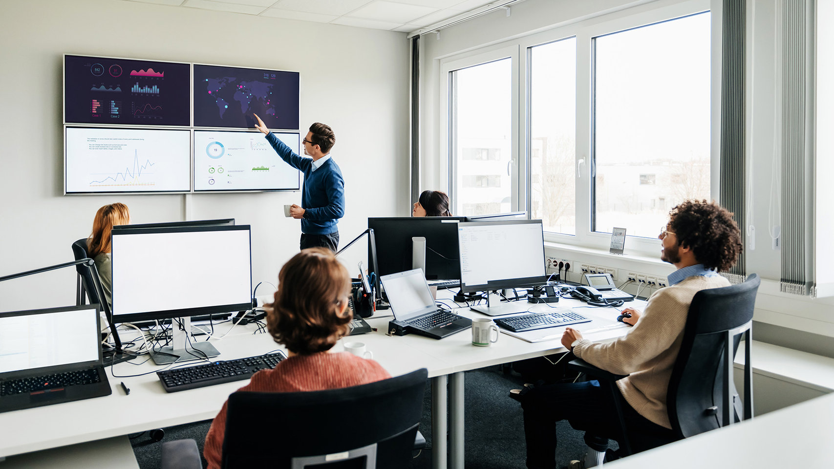 Business manager discussing data displayed on monitors with colleagues