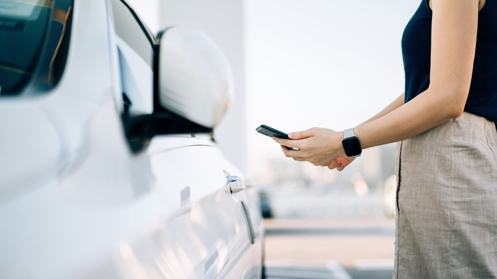 Close up of young Asian woman using mobile app device on smartphone to unlock the doors of her car-in a car park