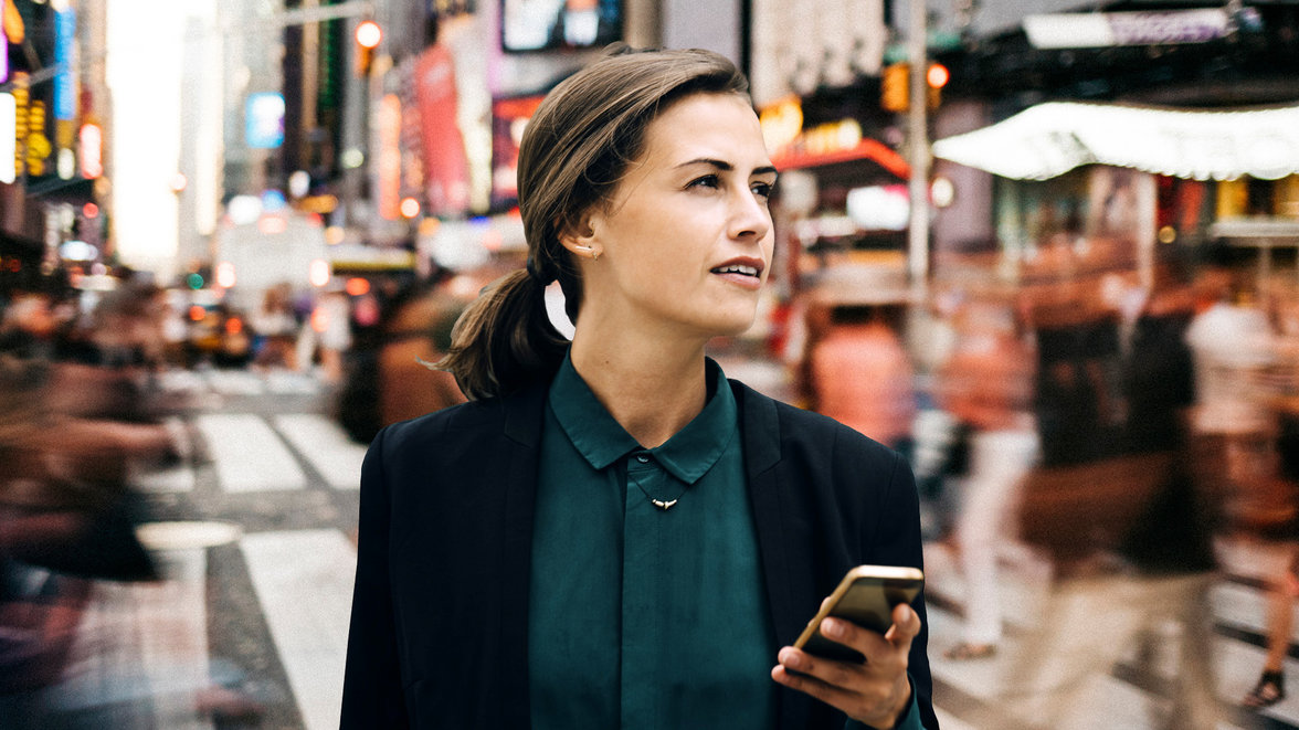 confident businesswoman looking away while holding smart phone in city