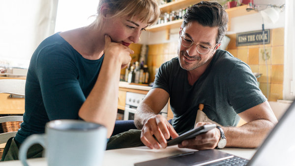 couple sitting at table in kitchen using smartphone