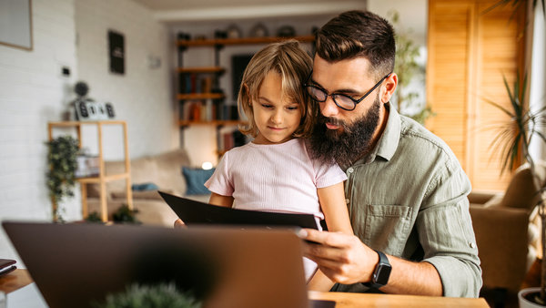 father-working-a-home-using-laptop-while-holding-his-daughter-in-his-laptop