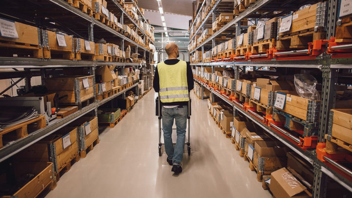 rear view of male worker pushing trolley in aisle at warehouse