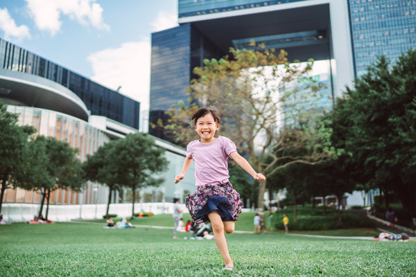 Happy kid in a green park with a tall building behind