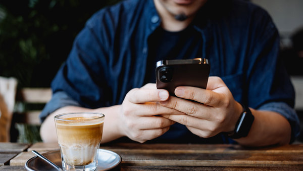 man sitting at a table in cafe using smartphone while having a cup of coffee