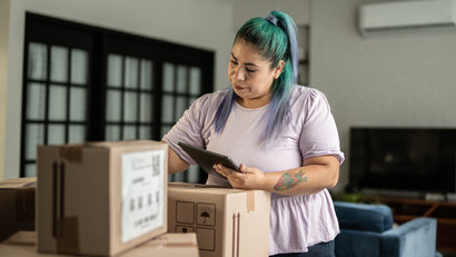 adult woman checking cardboard boxes while using digital tablet