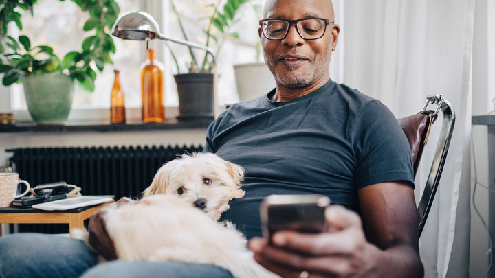 img-full-smiling-retired-senior-male-using-smart-phone-while-sitting-with-dog-in-room-at-home