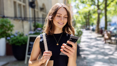 Smiling young woman with smartphone walking on the street