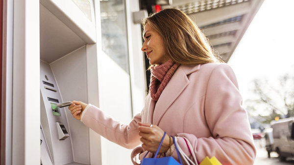 Young woman using ATM machine while holding shopping bags - ATM management