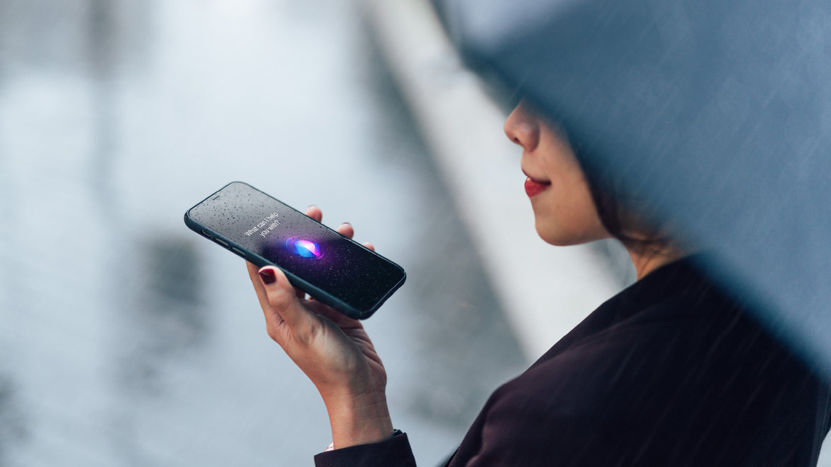 Woman using voice assistant on smartphone in the rain for AI In Banking Podcast: Harnessing AI and hyperautomation for banking