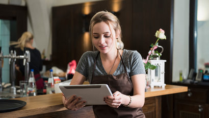 A young woman wearing an apron using a tablet in a restaurant.
