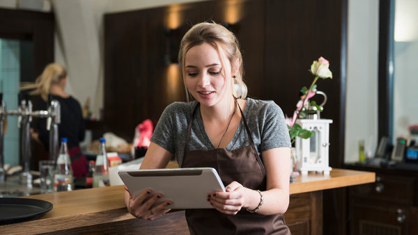 Young woman in apron using tablet at restaurant