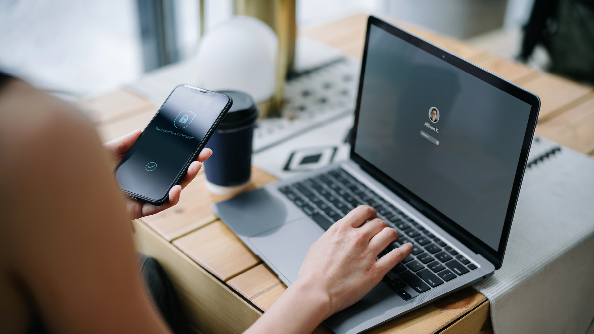 Young businesswoman working on desk logging in to her laptop and holding smartphone on hand with a security key lock icon on the screen