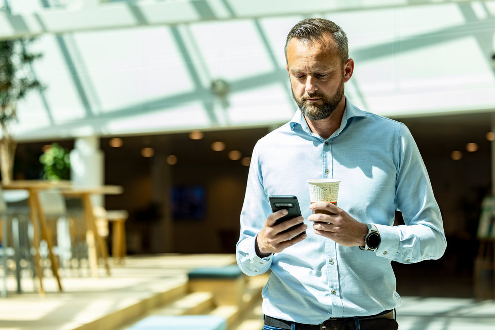 Man using his phone and holding a coffee