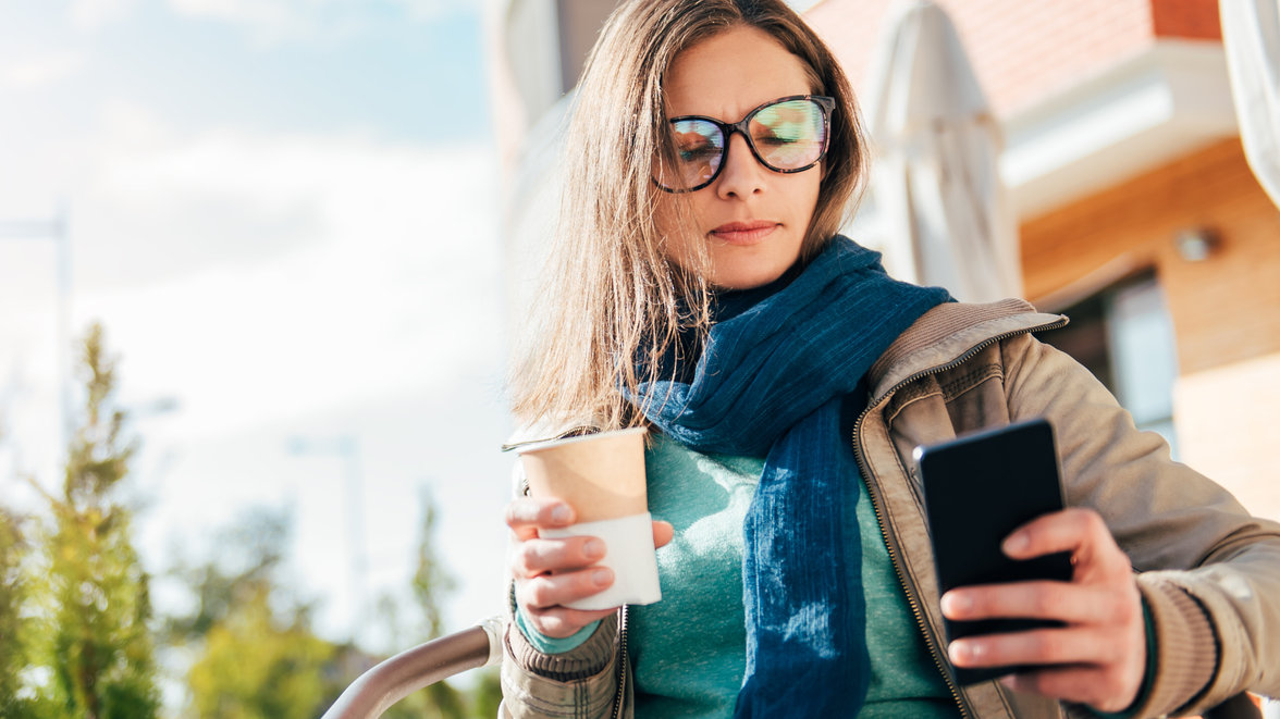 woman with mobile and coffee in hand