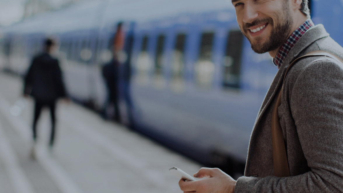 Man smiling while holding mobile phone in a train platform