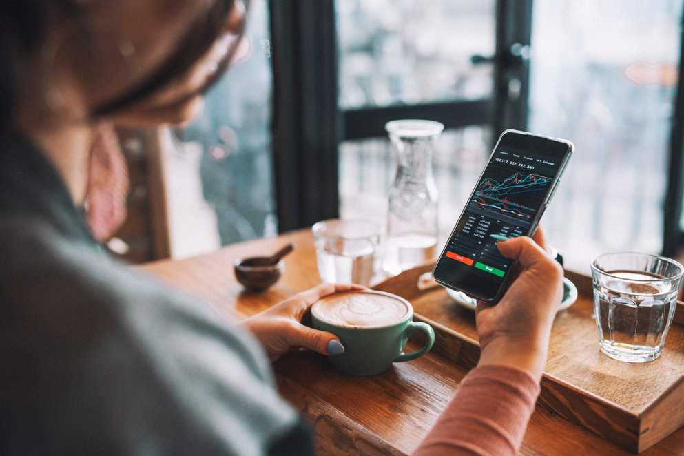 Woman using smartphone to buy cryptocurrency at a coffee shop