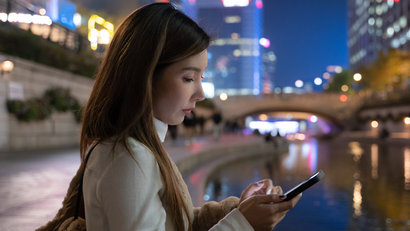 Asian woman using a smartphone sitting at Cheonggyecheon stream river park