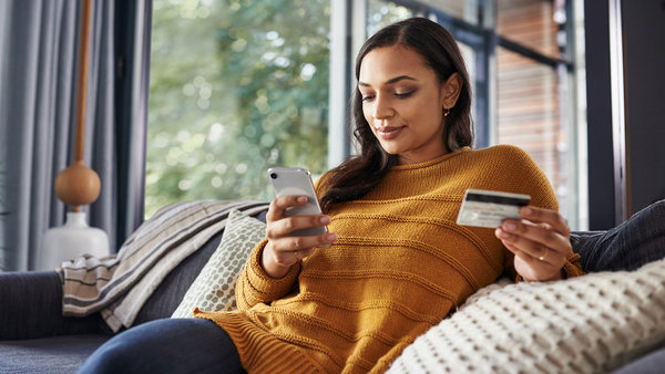 Belle jeune femme utilisant son téléphone portable et sa carte de crédit tout en bénéficiant des paiements en ligne optimisés de Worldline.