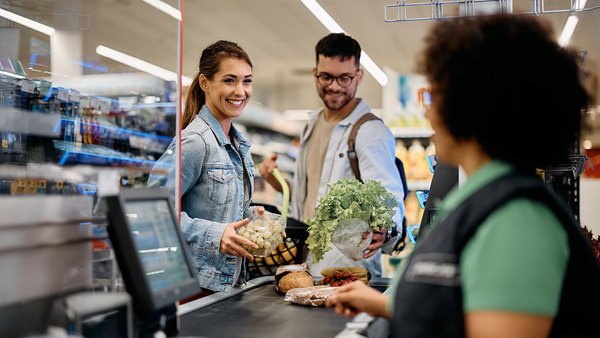 couple talking to cashier while putting groceries on checkout counter