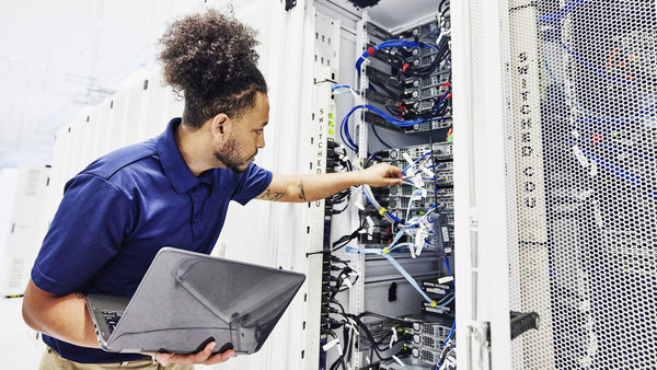 Medium shot of male IT profession using laptop while working on server in data center