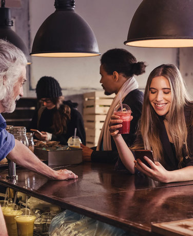 Ung kvinde sidder i en bar og får en rød smoothie mens hun kigger på sin telefon. 