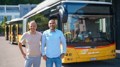 Zwei Mitarbeiter von Postauto, die vor einem PostAuto stehen