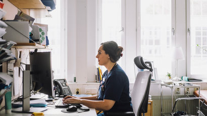 Side view of focused female healthcare worker using computer while sitting on desk in clinic