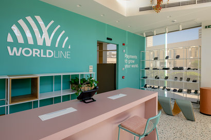 worldline logo on wall with a desk in front and different styles of payment machines on a shelf