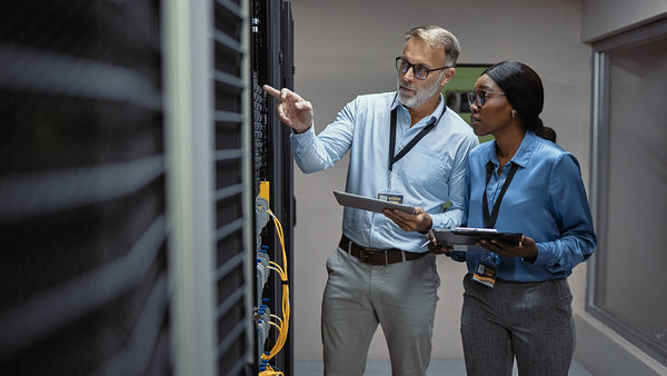 two IT technicians checking on working databases inside a dark server storage room
