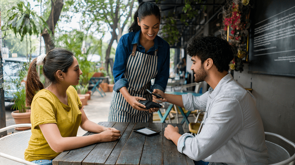 A man paying by card for both his and his female company orders at a cafe terrace.