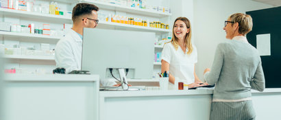 two pharmacy employees and a customer are gathered at the pharmacy counter.