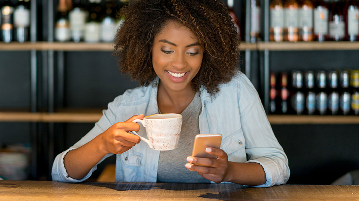 a woman drinking coffee whilst looking at her mobile phone