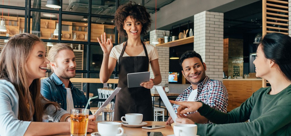Young african american woman waitress taking orders from Gen Z clients in cafe
