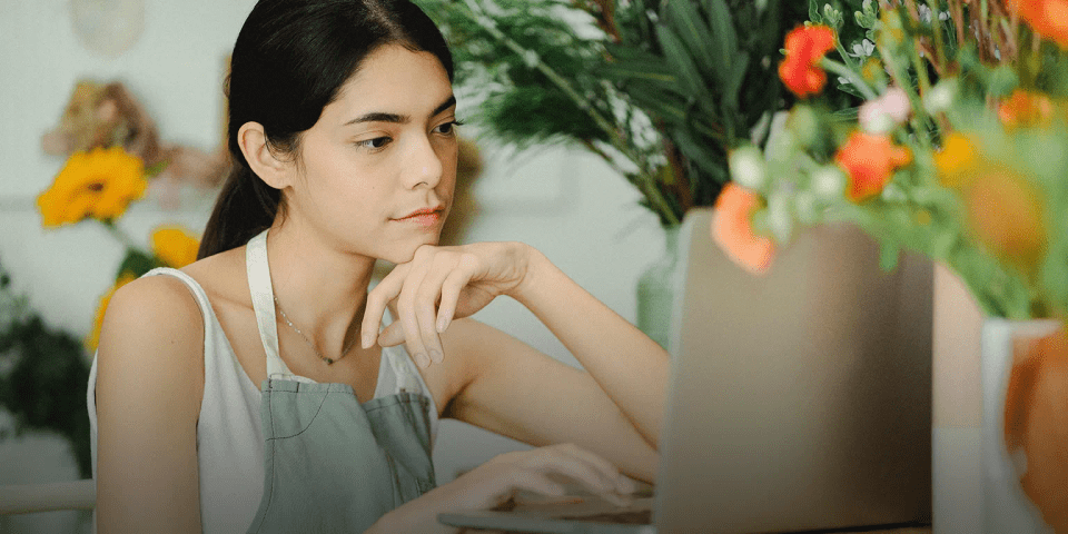 en kvinde med forklæde på sidder og kigger på sin computer i en blomsterforretning