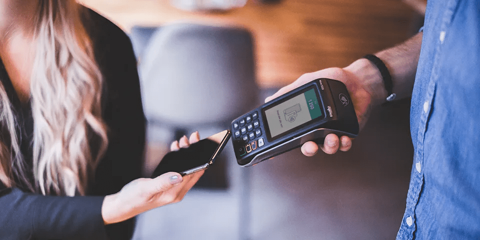 Kvinna betalar med sin mobiltelefon mot en Worldline kortterminal