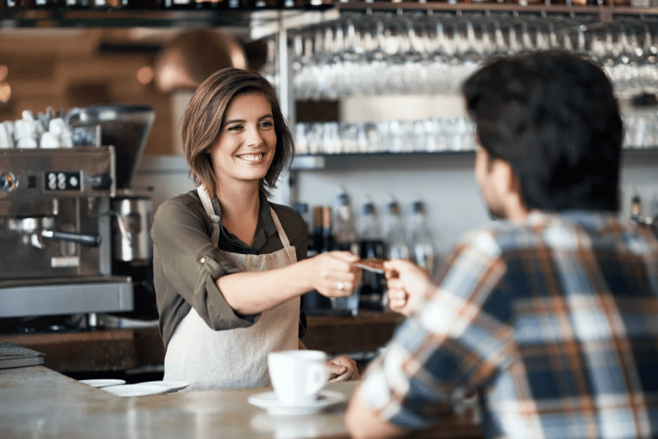 Barista tar imot kort fra en mannlig kunde som kjøper kaffe over disk