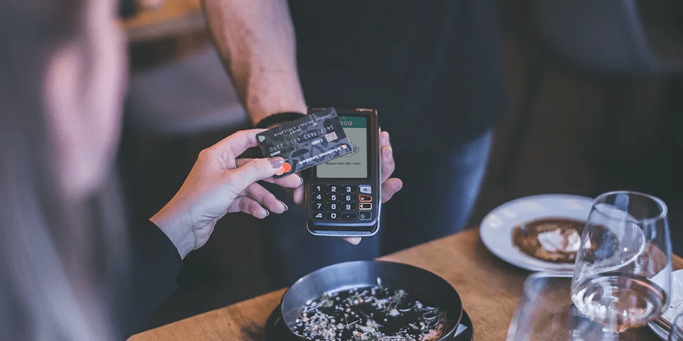 Mies pittää korttimaksupäätettä, nainen maksaa pankkikortilla ravintolassa