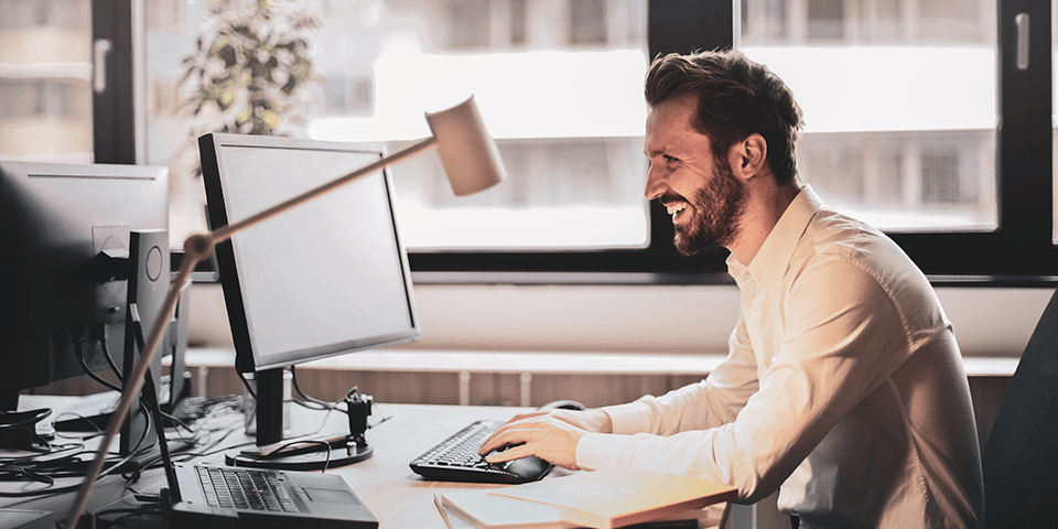  en mann sitter på kontoret sitt og smiler foran en skjerm