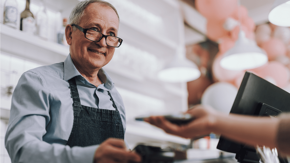 en gammel mand smilet sort til sin kunde som er ved at betale på en trådløs terminal